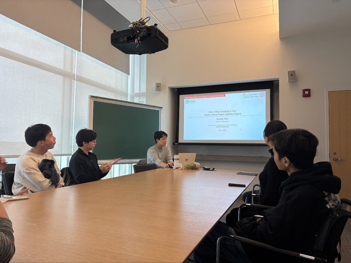 A speaker presenting a slide titled Give Vibe Coding a Try to attendees seated around a seminar table