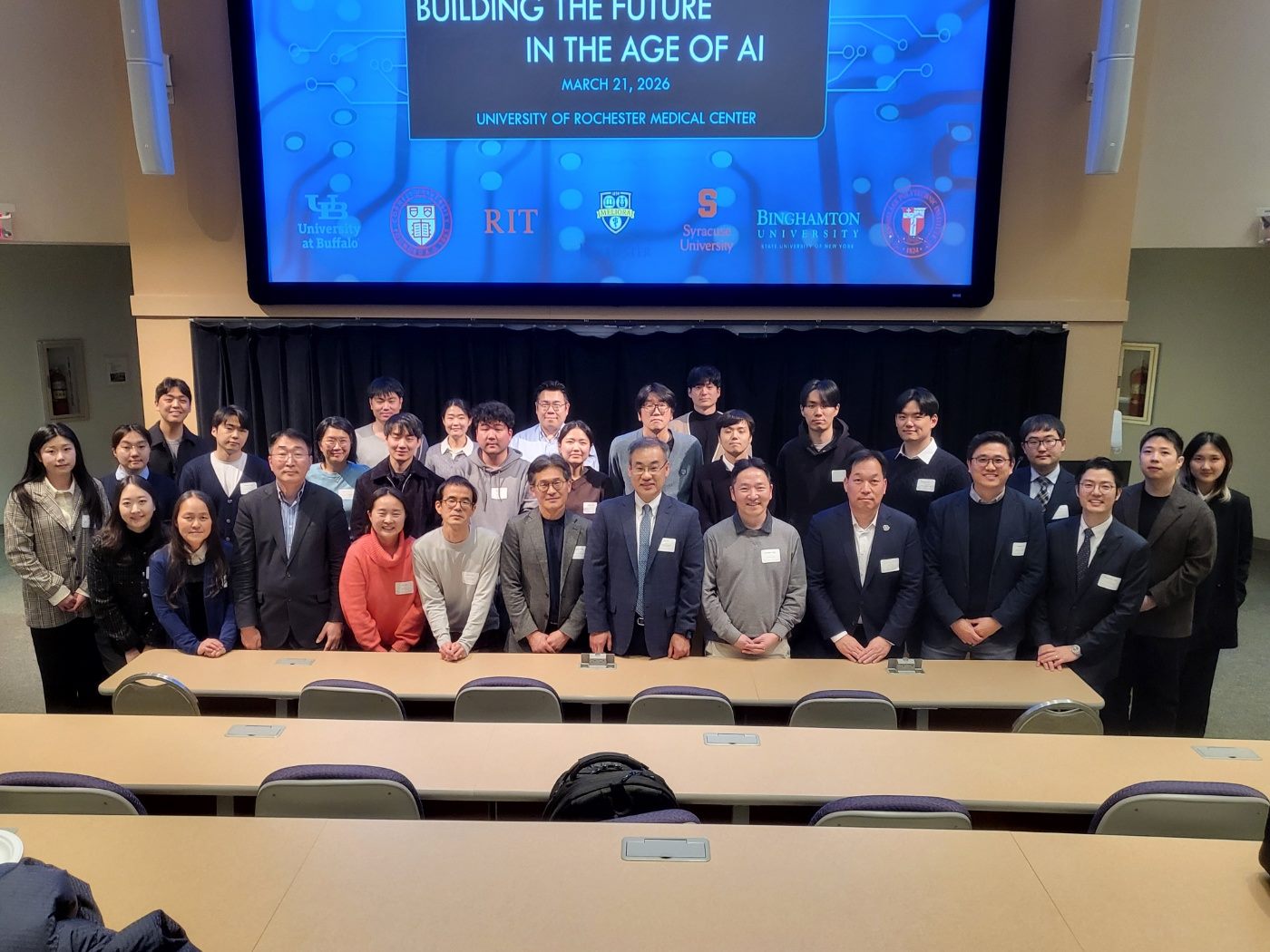 Around thirty-five attendees posed together in an auditorium beneath the symposium title slide