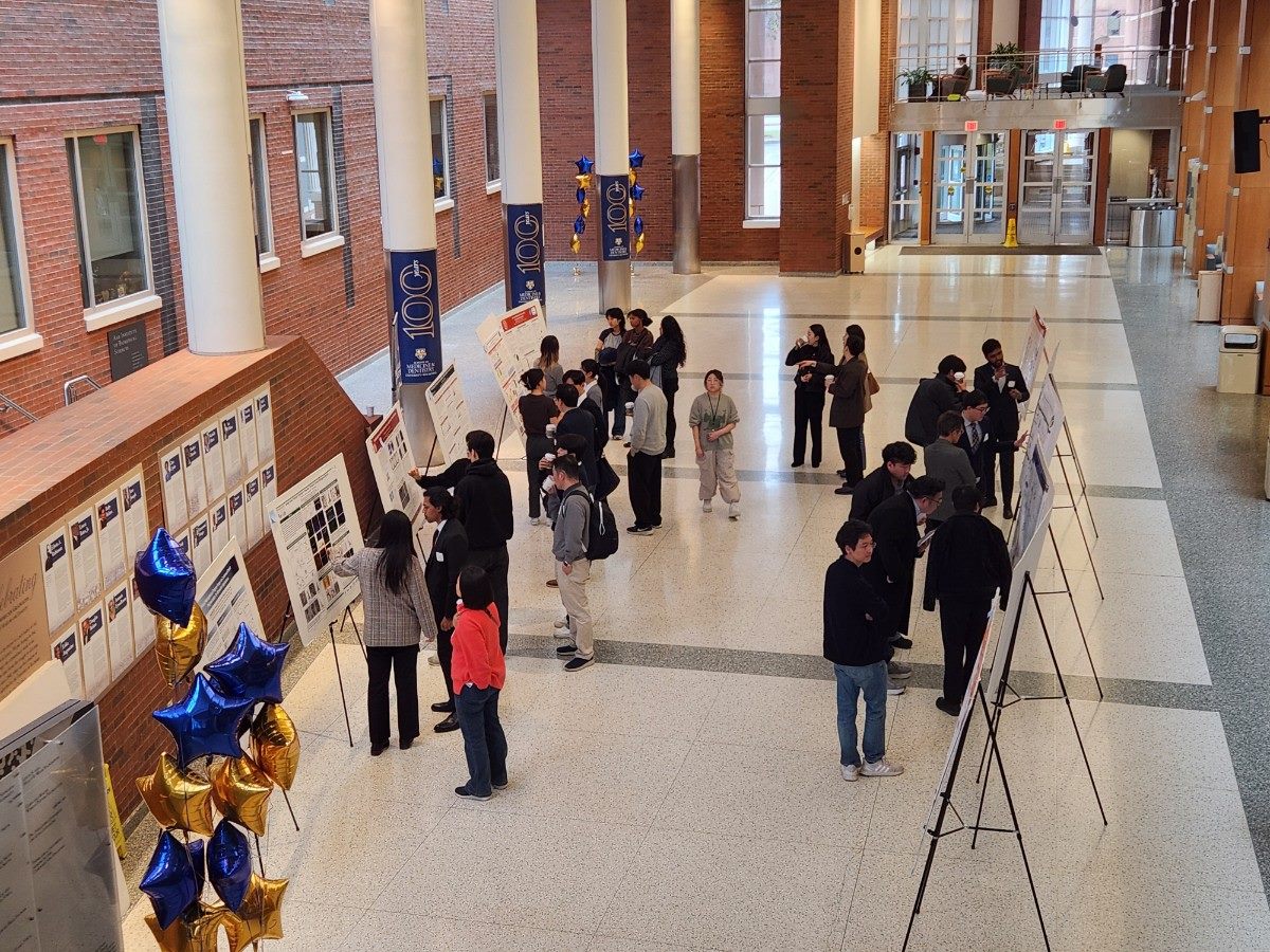 Attendees viewing research posters on easels in a large atrium, seen from a balcony above